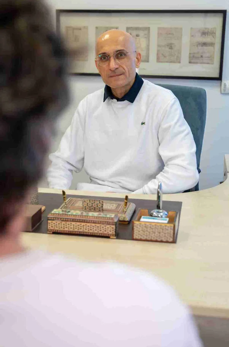 Dr. Salman listening to a patient, seen from behind, across his desk during a consultation