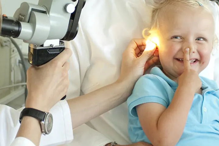 Smiling toddler having an ear examined with an otoscope