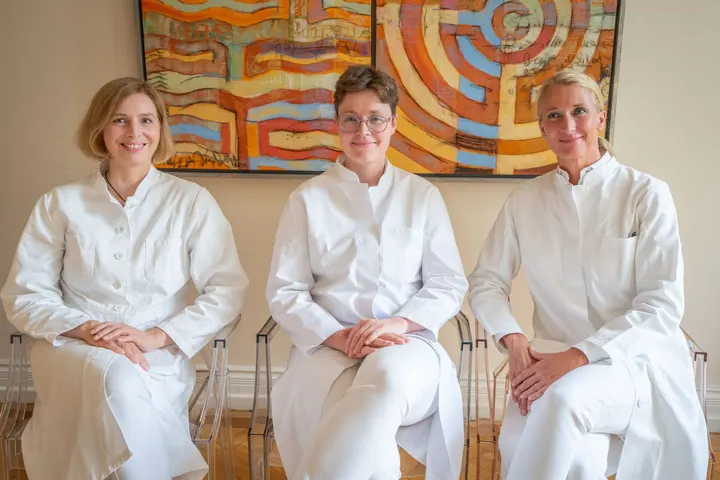 The practice’s three ENT doctors in white coats, seated in front of a colourful painting